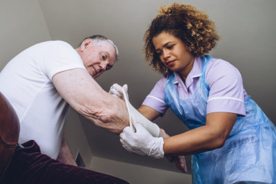 Caregiving nurse treating senior mans arm